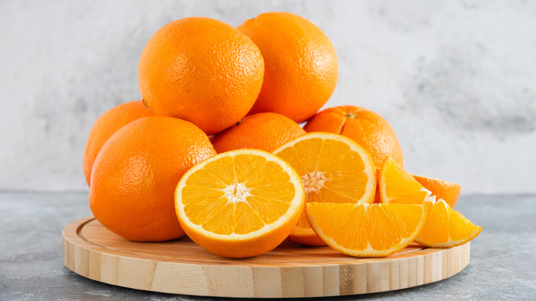 Several oranges, whole and sliced, on cutting board