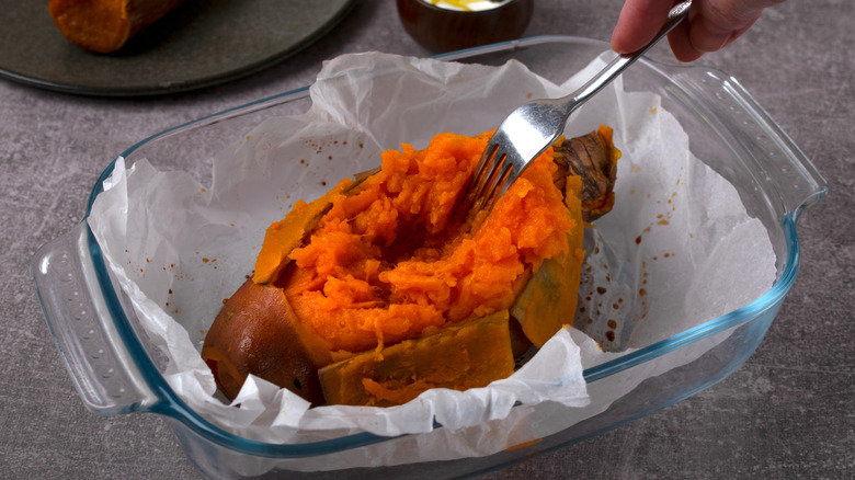 Person sticking a fork into a baked sweet potato