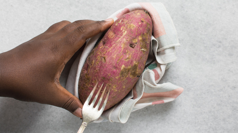 Person piercing an uncooked sweet potato with a fork