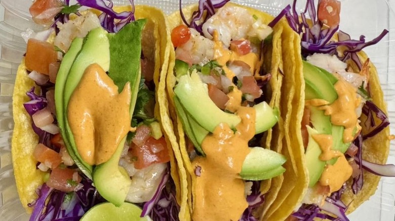 Three shrimp tacos with sauce on plate