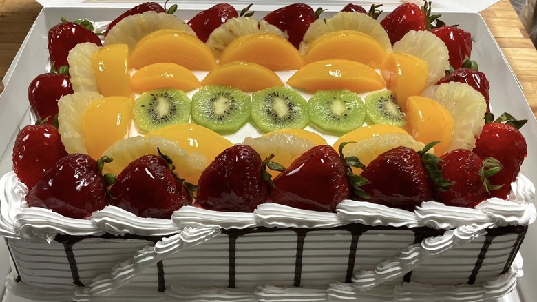 Rectangular cake topped with cream and fresh, glossy fruits