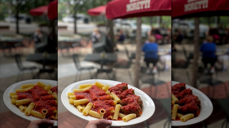 Hand holding plate of pasta in front of Tufano's outdoor seating area