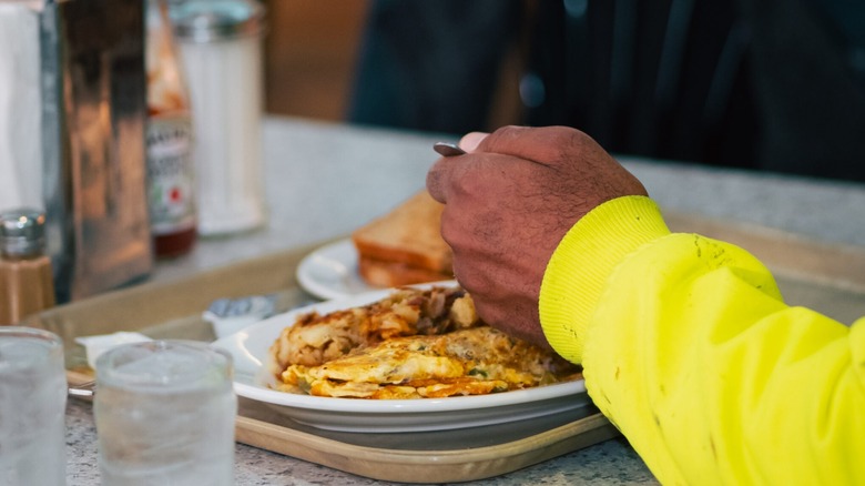 Unidentified person's hand with Yellow sweatshirt and omelet on a tray