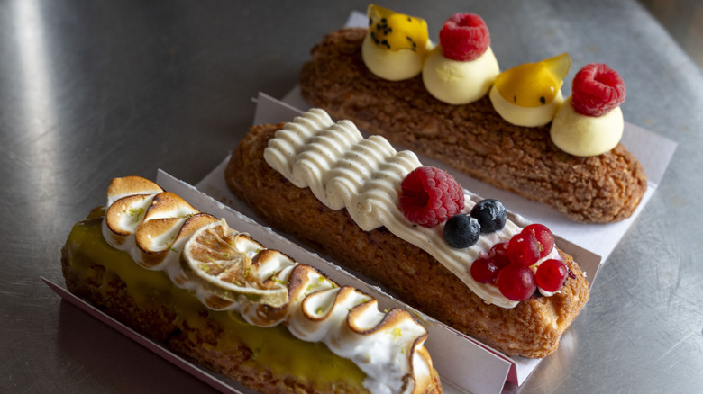 Three eclairs topped with toasted meringue, cream, and fresh fruits
