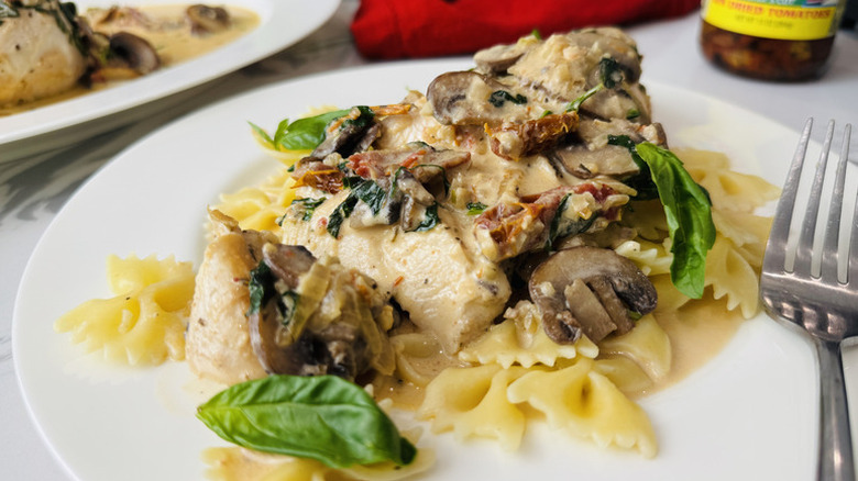 Plate of creamy mushroom and sun-dried tomato chicken, served over pasta