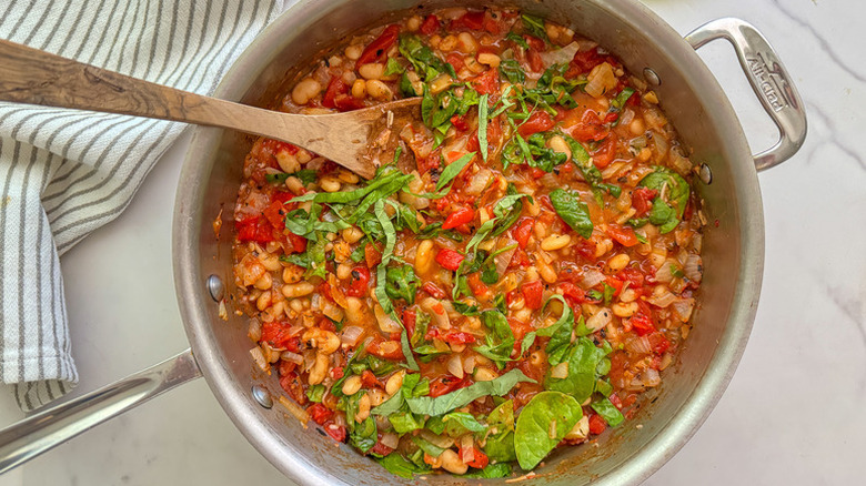 White bean and tomato stew in pot, garnished with basil