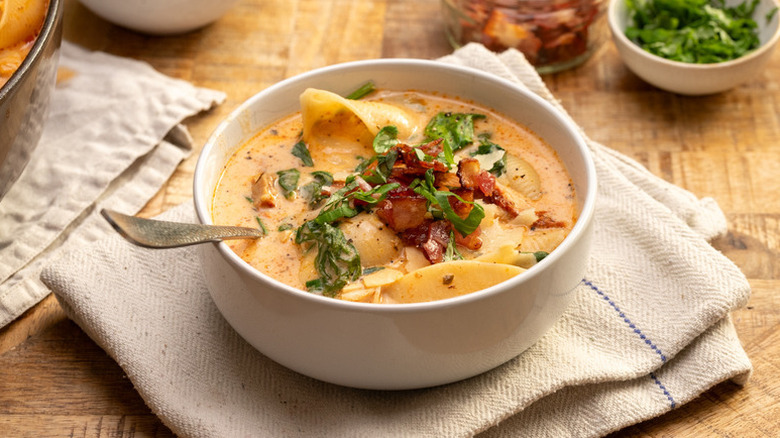 Bowl of creamy chicken and pasta soup, garnished with basil and crispy bacon