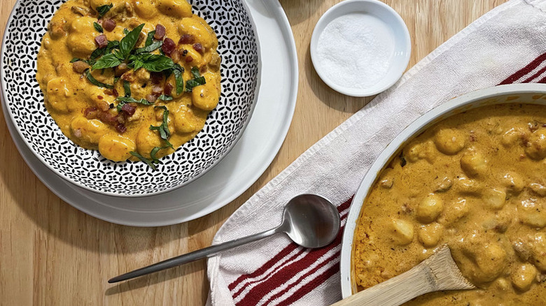 Creamy tomato gnocchi served into bowl and garnished with pancetta and basil