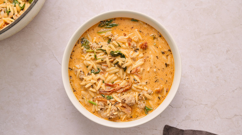 Creamy tomato, spinach, and sausage orzo soup in bowl