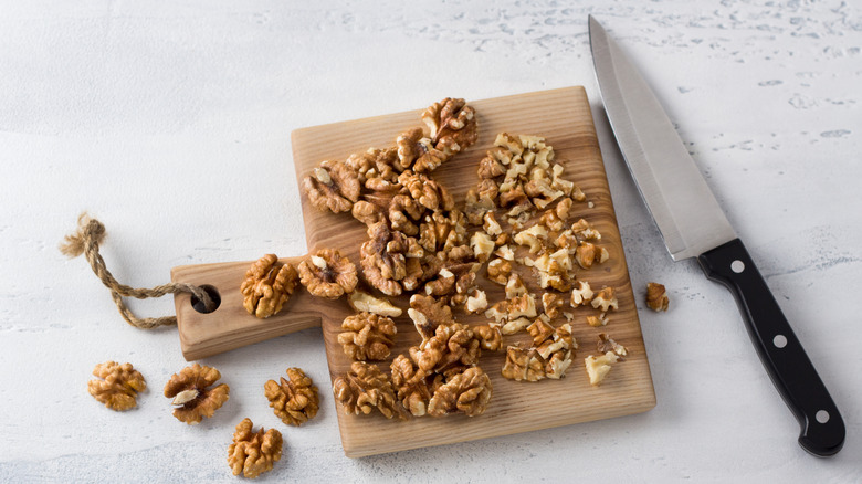 Knife beside cutting board topped with whole and chopped walnuts