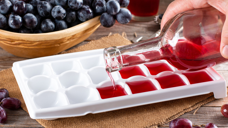 person pouring liquid from bottle into ice cube tray