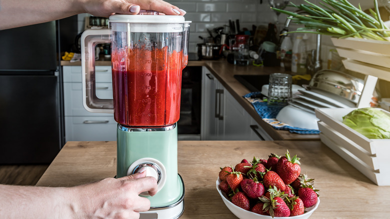 person blending strawberries; a bowl of strawberries sits on counter