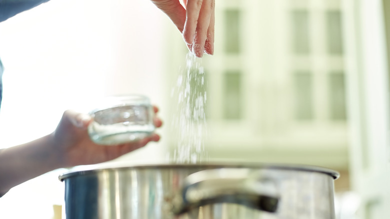 person sprinkling salt into pot on stove