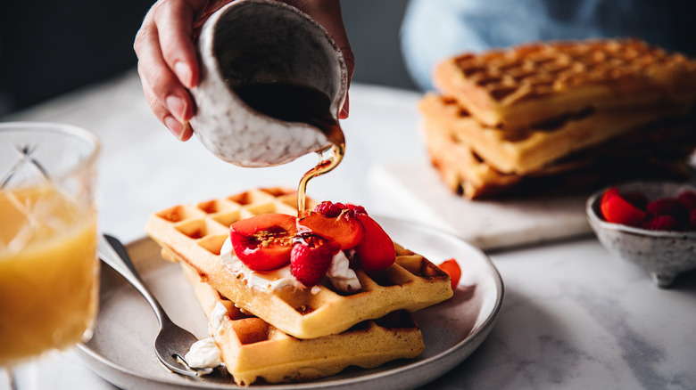 Close-up of a female hand pouring syrup on waffle