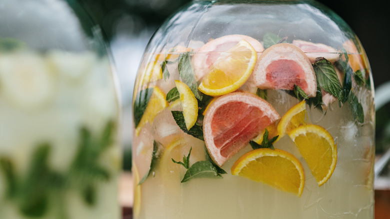 Jar of liquid being infused with herbs and citrus slices