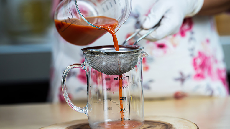 Woman straining liquid through a fine-mesh sieve into a glass measuring cup