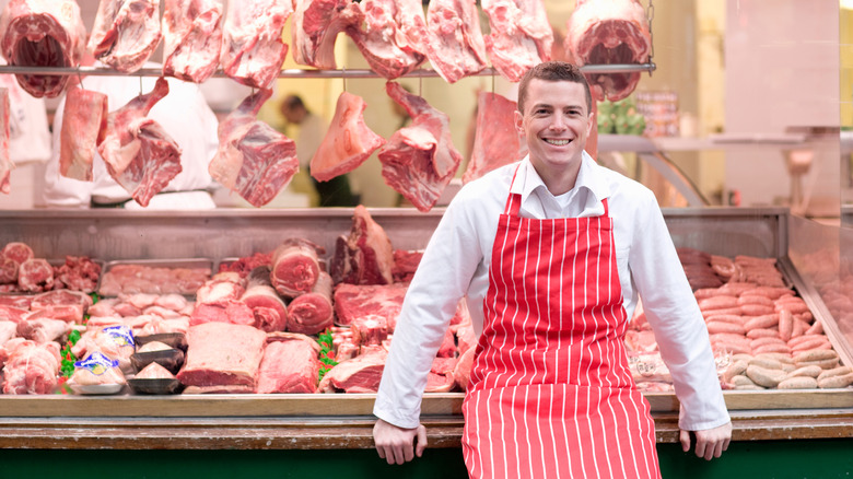 Smiling butcher with cuts of meat in background