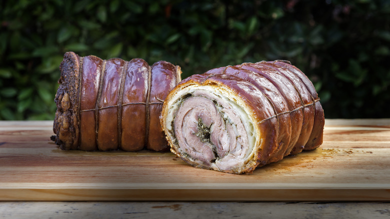 An Italian-style rolled pork roast, or porchetta, cut in half on a wooden cutting board