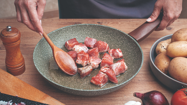Person stirring cubed pork with a wooden spoon in a nonstick skillet