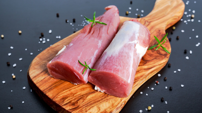 Two pieces of raw pork tenderloin on a wooden serving board