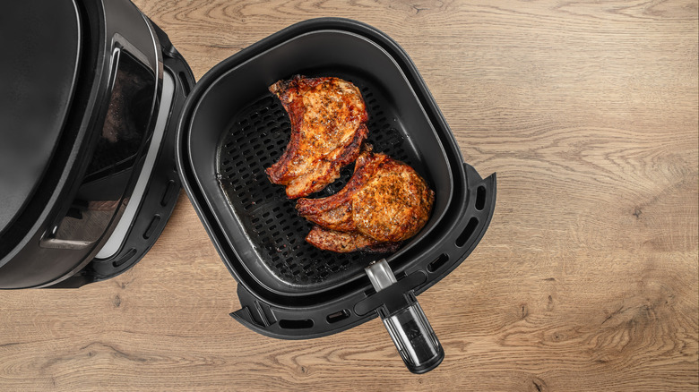 Two browned and seasoned bone-in pork chops in the basket of an air fryer