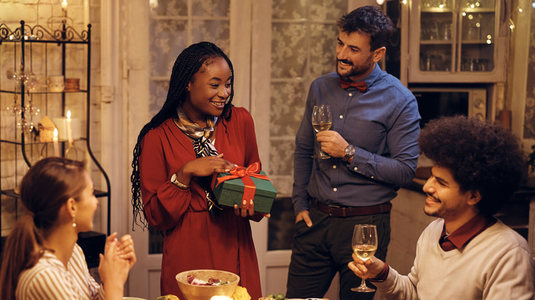 Woman giving wrapped gift to friend over holiday feast