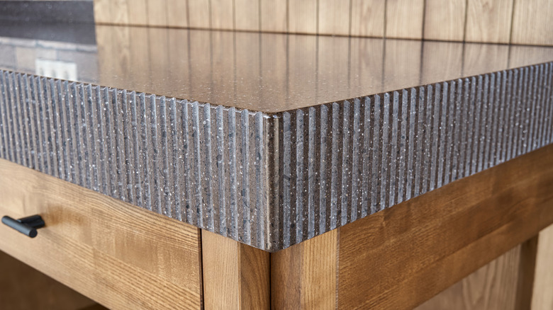 A wooden kitchen island with a thick, dark stone countertop featuring a decorative, ridged edge