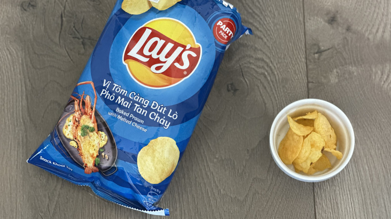 Overhead image of bag of Lay's Baked Prawn with Melted Cheese flavored potato chips with small white ramekin filled with chips