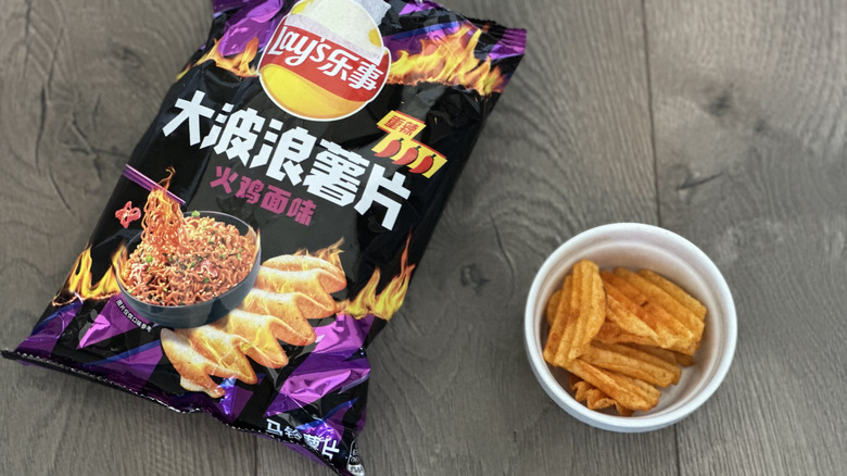 Overhead image of bag of Lay's Hot Chicken Noodle flavored potato chips with small white ramekin filled with chips