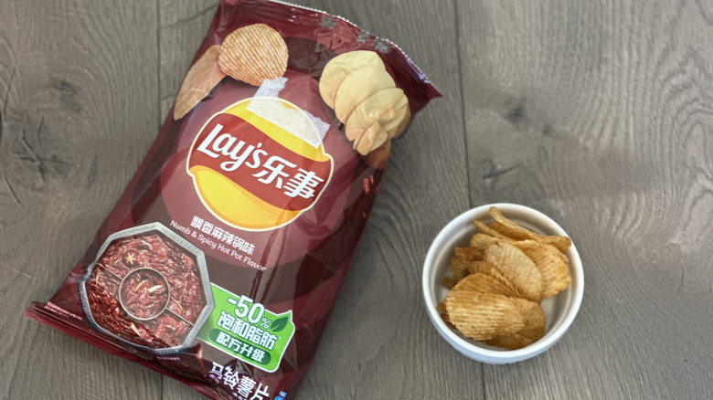 Overhead image of bag of Lay's Numb & Spicy Hot Pot flavored potato chips with small white ramekin filled with chips