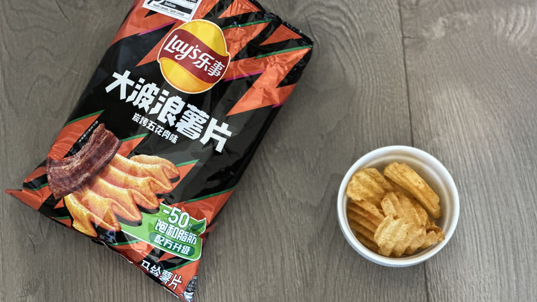 Overhead image of bag of Lay's Grilled Pork flavored potato chips with small white ramekin filled with chips