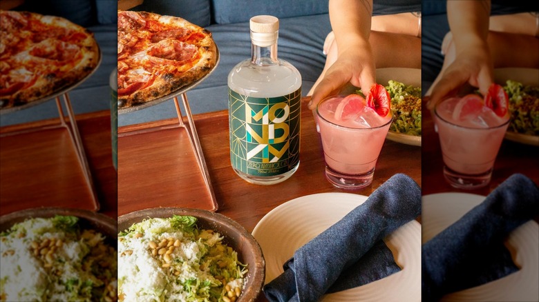 Bottle of Monday zero alcohol gin on table with drink, salad, pizza, white plate and napkin