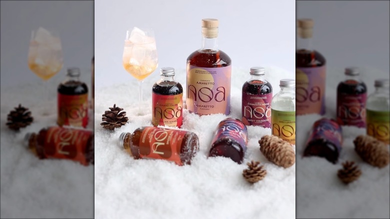 Bottles of NOA spirits on snowy table, wine glass beside