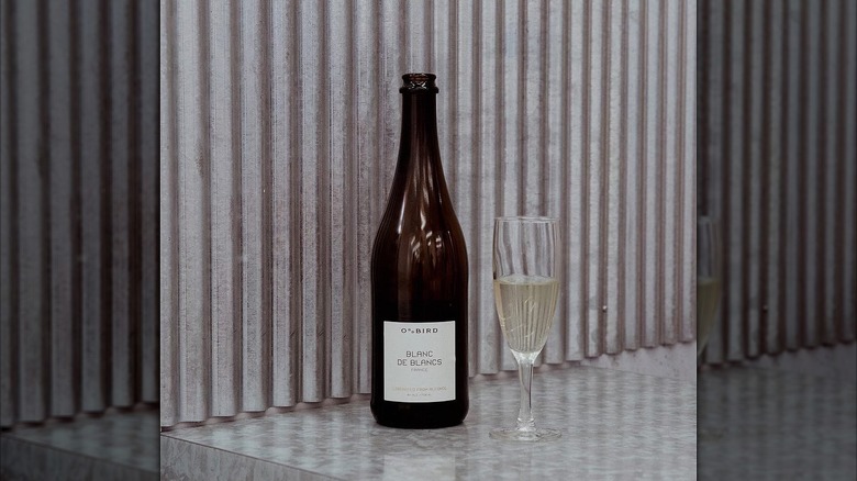 Bottle of Oddbird Blanc de Blancs next to glass of wine on grey surface