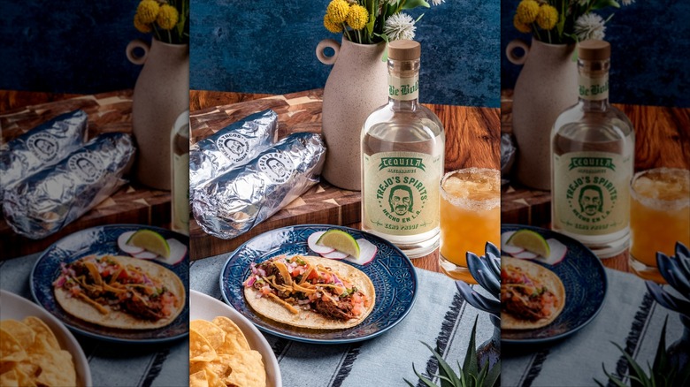 Bottle of Trejo's Spirits tequila alternative behind soft taco on plate, drink beside