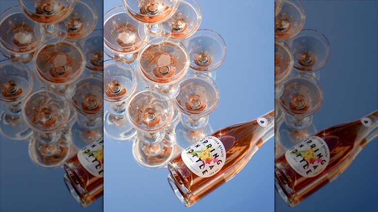 Bottle of Wolffer Spring in a Bottle Sparkling Rosé next to glasses of rosé on blue background