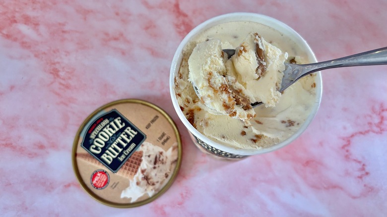 Trader Joe's Cookie Butter ice cream in spoon above quart on pink marble suraace