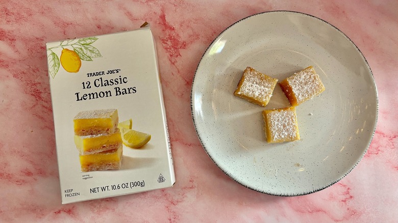 Trader Joe's lemon bars on white plate next to box on pink marble surface