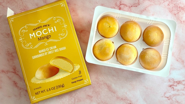 Mango mochi in plastic holder next to package on pink marble surface
