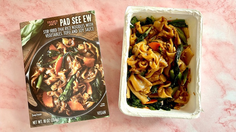 Pad see ew in container next to package on pink marble surface