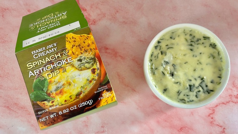 Trader Joe's spinach artichoke dip box next to dip in white ramekin on pink marble surface