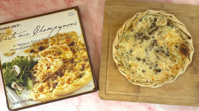 Trader Joe's Tarte aux Champignons on cutting board next to box on pink surface