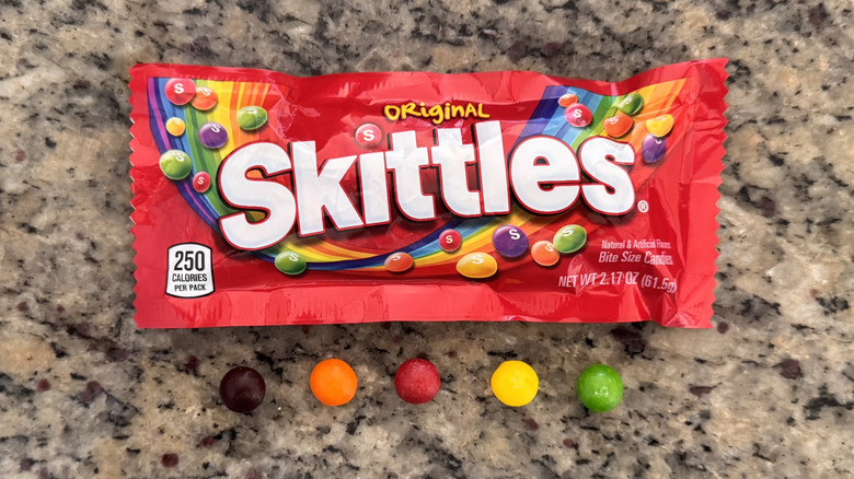 bag of skittles with several candies beside it on counter