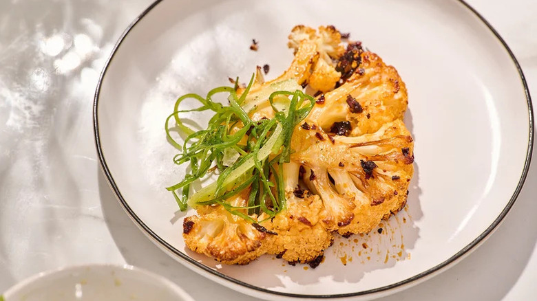 Chili crisp-baked cauliflower steaks on a white dish with a green garnish