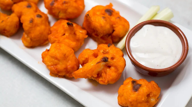Plate with baked buffalo cauliflower wings and a creamy dipping sauce