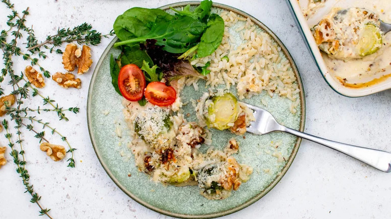 Plate with Brussels sprouts au gratin with rice and a salad surrounded by fresh thyme and walnuts