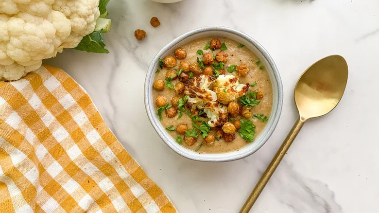 Roasted garlic cauliflower soup with a spoon and head of cauliflower