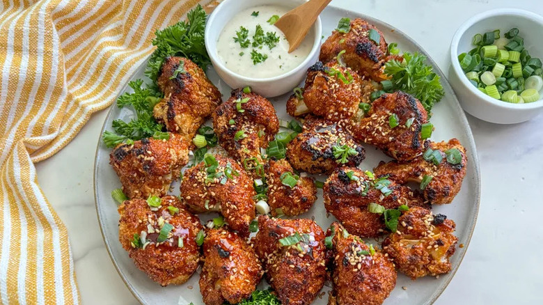 Plate with sticky garlic cauliflower wings with scallions and a creamy dipping sauce