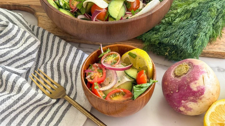 Small and large wooden bowls filled with turnip salad surrounded by ingredients