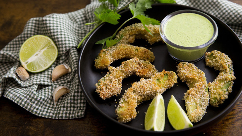 Breaded avocado fries on plate with creamy dip and lime wedges